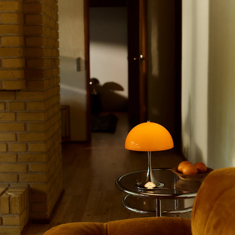 Louis Poulsen Panthella 250 portable lamp in orange on a glass side table beside a sofa in a softly lit interior