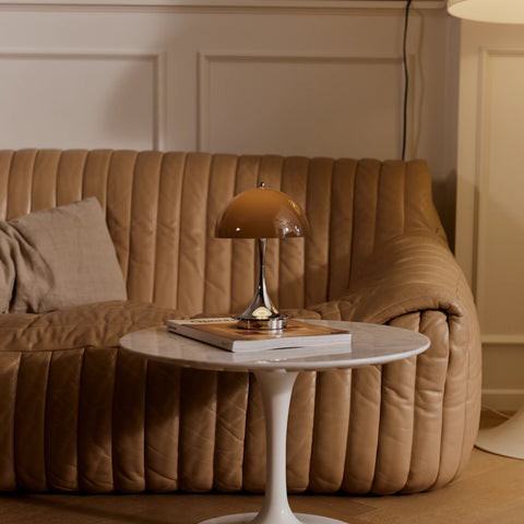 Louis Poulsen Panthella 160 portable lamp in brown sitting on a marble side table beside a leather sofa