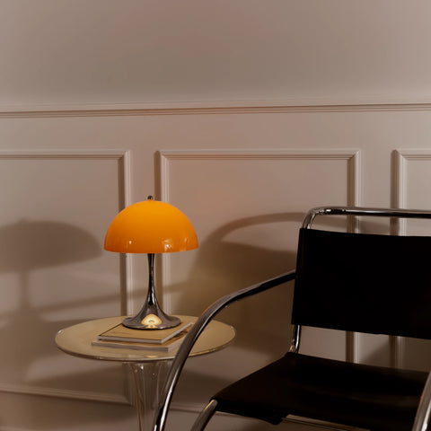 Louis Poulsen Panthella 250 portable lamp in orange placed on a glass side table beside a modern chair
