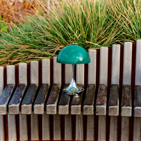 Louis Poulsen Panthella 160 portable lamp in green placed on a wooden bench in an outdoor garden setting