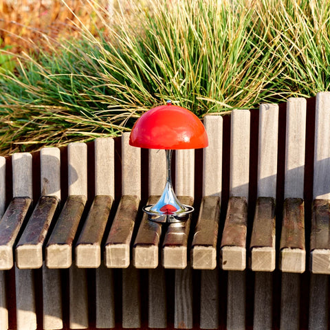 Louis Poulsen Panthella 160 portable lamp in red placed on a wooden bench in an outdoor setting