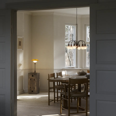 Louis Poulsen PH 1/1 Chandelier in blackened brass finish hanging above a rustic wooden dining table with rush-seat chairs in a sun-filled Scandinavian dining room