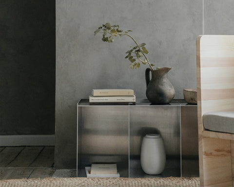 Frama Rivet Case in Aluminum, metal case against a concrete wall holding books and a jug of branches, a vase on the floor
