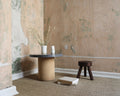 Frama AML Stool in Dark Pine, dark stool on a sisal rug beside a stone pedestal table and dried grasses in a stripped room