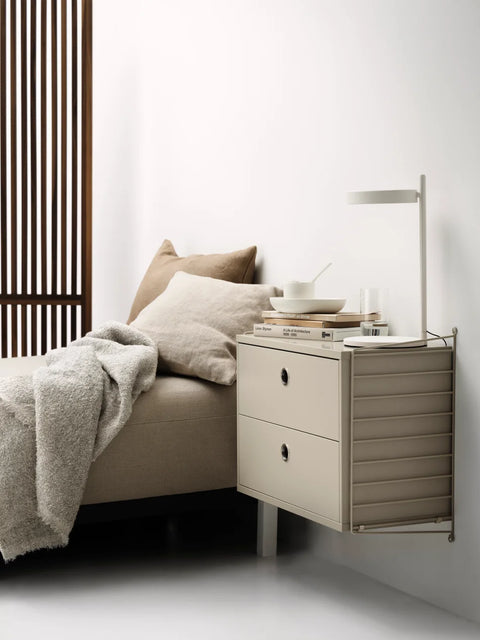 Beige String® System chest of drawers with two drawers used as a bedside table in a minimalist bedroom