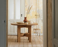 Frama Farmhouse Trestle Table in Natural Oak, round oak table with a vase and stacked bowls seen through a doorway, stool alongside