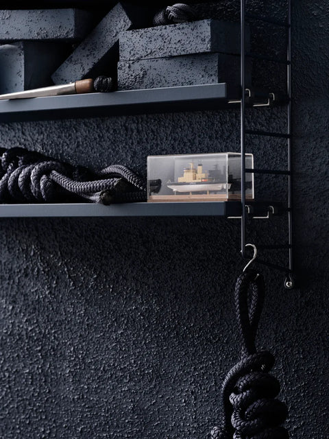 Close-up of dark blue String® Pocket shelf against textured wall with nautical rope and decorative objects