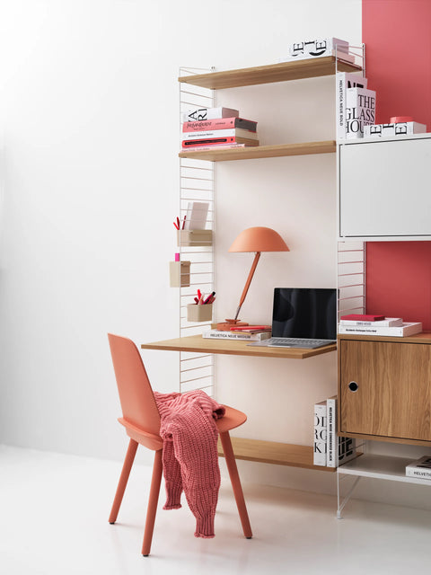 String Furniture Work Desk in oak finish with modular shelving, Scandinavian workspace styled with coral chair and desk lamp.