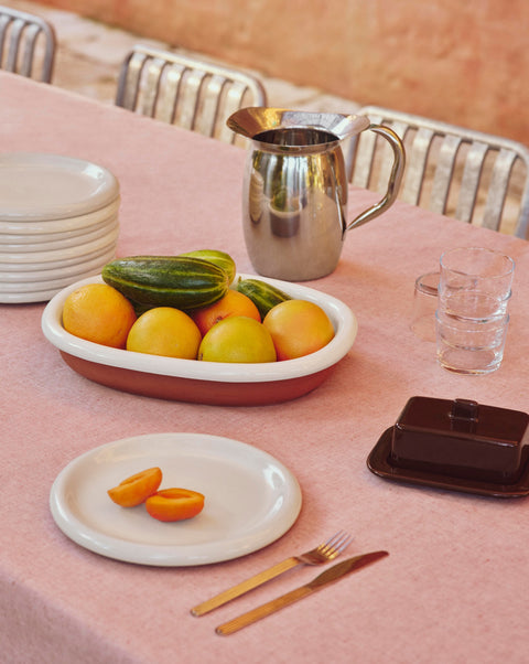 HAY Barro Oval Dish, Large, Off-White, glazed terracotta oval serving dish, holding citrus on a pink tablecloth with a steel jug and butter dish