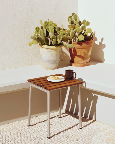 HAY Barro Plates, Ø18, Off-White, glazed terracotta side plate, on a teak stool by a white wall with potted cacti and a mug