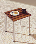 HAY Barro Plates, Ø18, Off-White, glazed terracotta side plate, holding a tart on a teak stool with a brown mug on pebbled paving