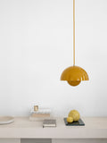 Flowerpot VP1 Pendant Light by &Tradition in Mustard Yellow above a minimalist shelf with lemons and stacked books.