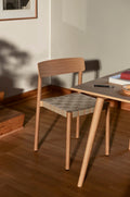 Betty TK1 Side Chair by &Tradition in oak with linen webbing beside wooden dining table in sunlit interior