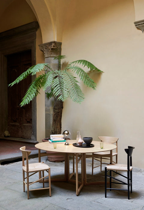 Drop Leaf HM6 table in oak by &Tradition styled with mix of dining chairs in Mediterranean courtyard