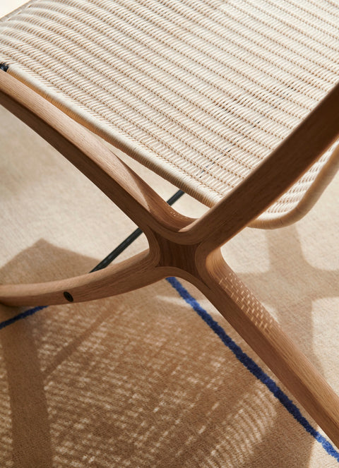 Detail of X HM10 by &Tradition showing paper cord seat and sculpted oak X joint with soft shadows across the rug
