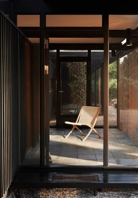 X HM10 Chair by &Tradition in oak with woven paper cord placed in a sunlit glass corridor connecting indoor and garden spaces