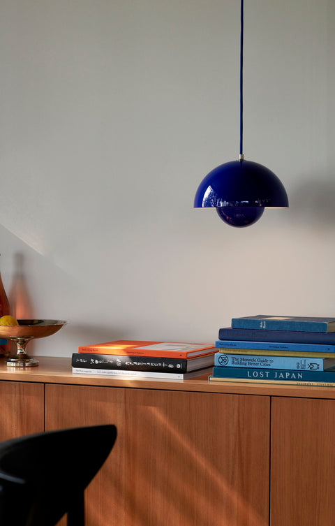 Flowerpot VP1 Pendant Light by &Tradition in Cobalt Blue styled above a wooden credenza with stacked books and decor.