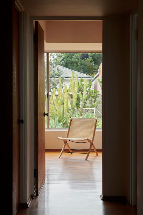X HM10 Chair by &Tradition in oak and paper cord framed by a hallway with a cactus garden view through the window