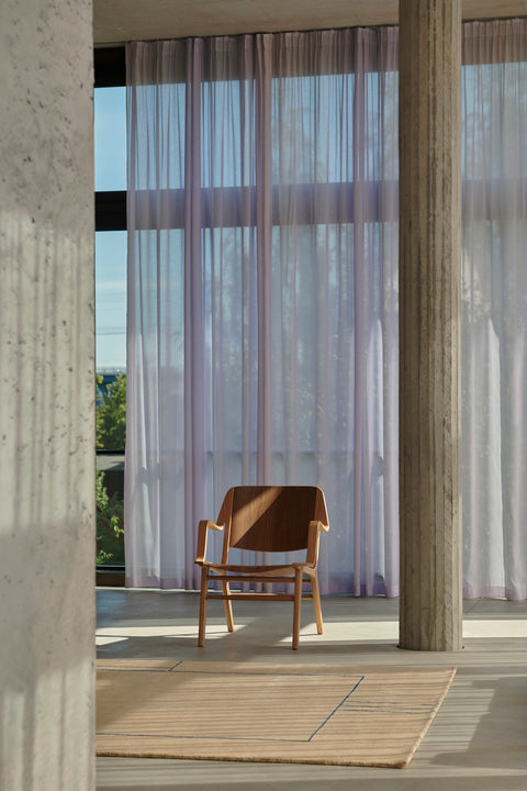 AX HM11 Lounge Chair by &Tradition in walnut and oak, styled in a modern interior with floor-to-ceiling curtains