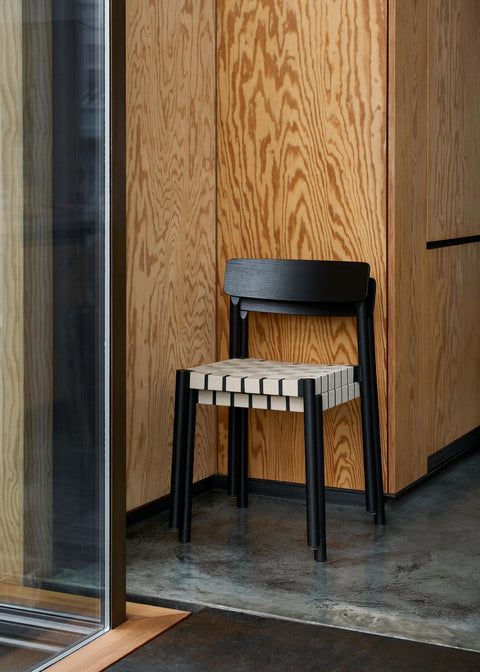Stacked Betty TK1 Side Chairs by &Tradition in black oak with natural webbing against plywood wall