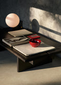 Dark stained oak Ita OS3 Coffee Table by &Tradition with a sculptural lamp, red bowl, and art books bathed in warm afternoon light.