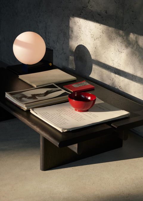 Dark stained oak Ita OS3 Coffee Table by &Tradition with a sculptural lamp, red bowl, and art books bathed in warm afternoon light.
