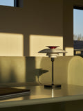 PH 80 Portable Lamp in white illuminated on a minimalist table in a warm living room setting by Louis Poulsen