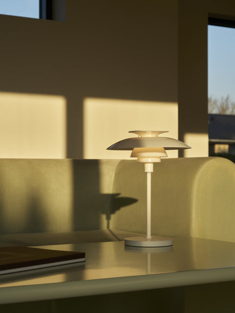 PH 80 Portable Lamp in white illuminated on a minimalist table in a warm living room setting by Louis Poulsen