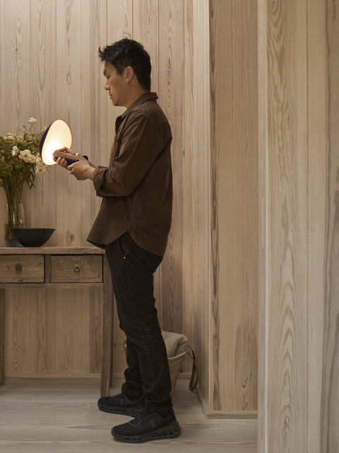 Designer adjusting the Rumee 220 Portable Lamp in a warm wooden interior.