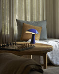 Rumee 220 Portable Lamp in Night Blue casting warm light over a wooden table with a chessboard.