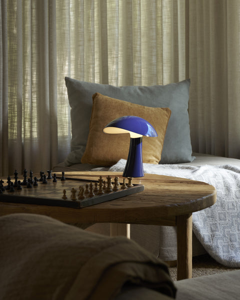Rumee 220 Portable Lamp in Night Blue casting warm light over a wooden table with a chessboard.