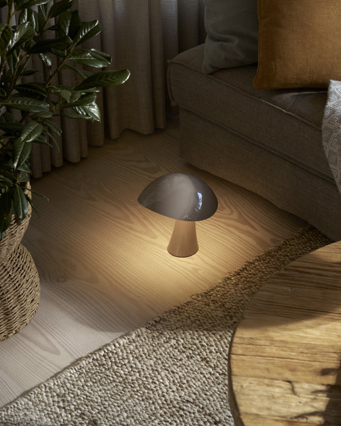 Louis Poulsen Rumee 220 Portable Lamp in Earth Grey illuminating a cozy living room corner.