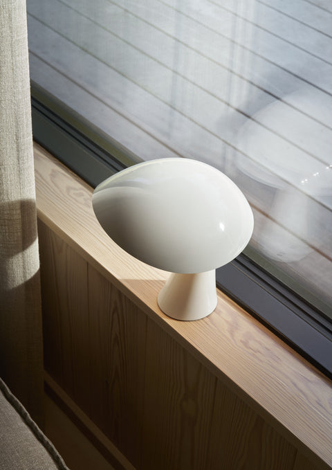 Rumee 220 Portable Lamp in Cloud White resting on a wooden windowsill with natural daylight reflection.
