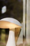 Louis Poulsen Rumee 220 Portable Lamp in Cloud White glowing softly beside a sunlit window.