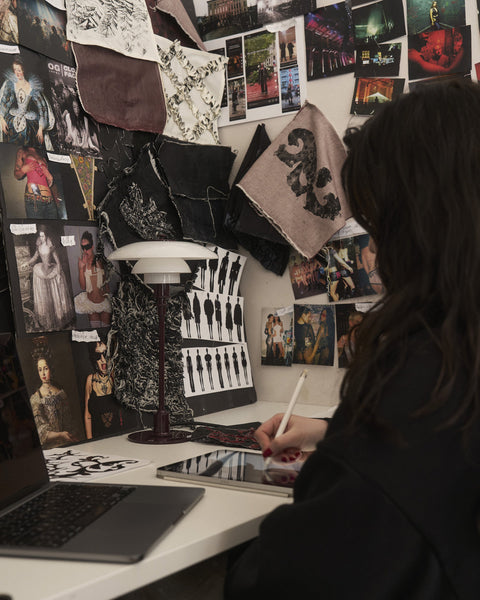 Louis Poulsen PH 2/1 Table Lamp in Glossy Burgundy on a studio desk as a designer sketches, against a collaged mood-board wall