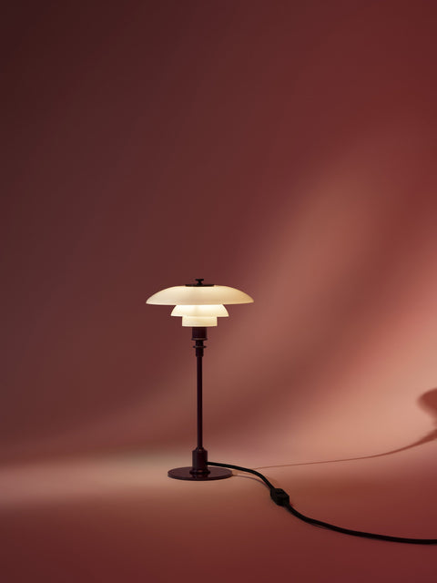 Louis Poulsen PH 2/1 Table Lamp in Glossy Burgundy, lit against a deep red draped backdrop