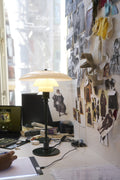 Louis Poulsen PH 2/1 Table Lamp in Glossy Deep Green, lit on a designer's desk beside a wall of pinned fabric swatches and sketches