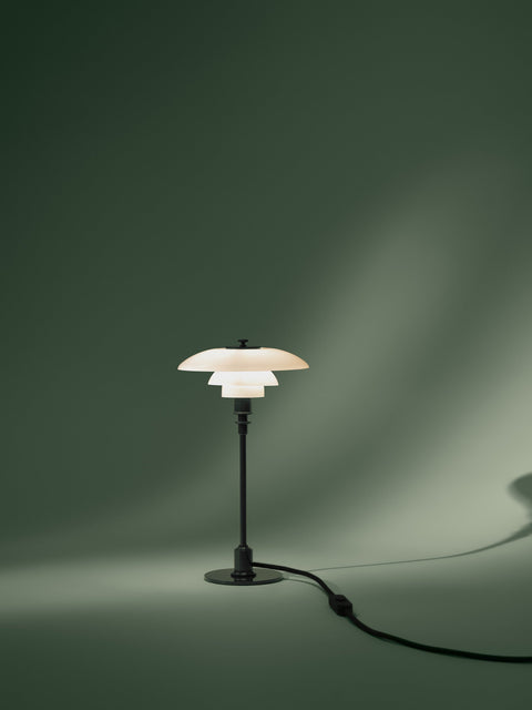 Louis Poulsen PH 2/1 Table Lamp in Glossy Deep Green, lit against a deep green draped backdrop with the cord trailing across the floor