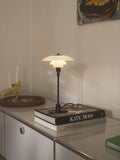 Louis Poulsen PH 2/1 Table Lamp in Glossy Deep Green, lit on a stack of art books atop a sideboard below a framed painting