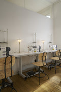 Two Louis Poulsen PH 3/2 Glass Table Lamps in Glossy Beige lit along a sewing atelier worktable with machines, wooden chairs and a plank floor