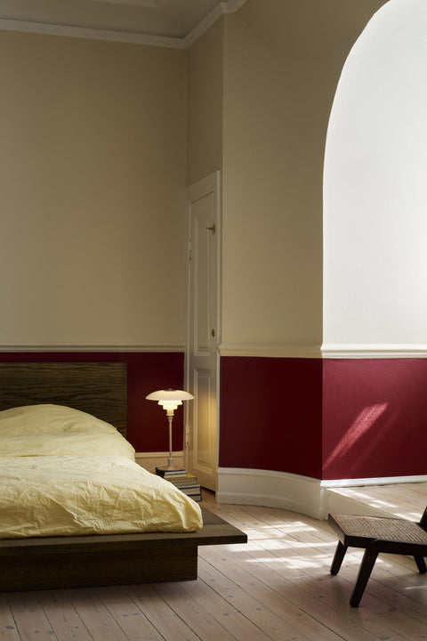 Louis Poulsen PH 3/2 Glass Table Lamp in Glossy Beige lit at a bedside, seen through a curved archway into a bedroom with a deep red painted dado