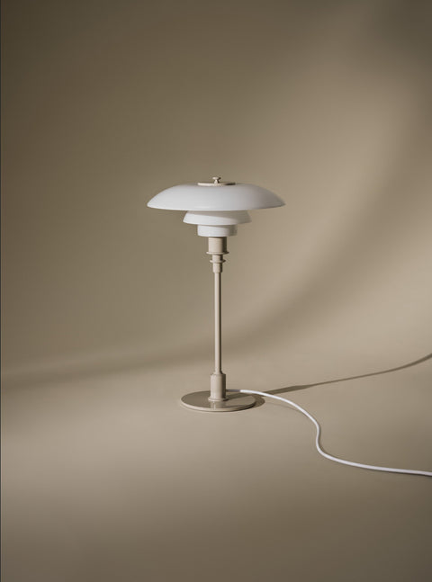 Louis Poulsen PH 3/2 Glass Table Lamp in Glossy Beige, unlit against a soft taupe draped backdrop with a white cord