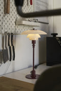 Louis Poulsen PH 3/2 Glass Table Lamp in Glossy Burgundy, lit on a kitchen counter beside a wall-mounted knife rack