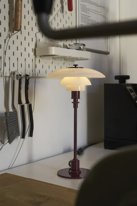 Louis Poulsen PH 3/2 Glass Table Lamp in Glossy Burgundy, lit on a kitchen counter beside a wall-mounted knife rack