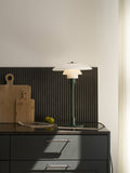 Louis Poulsen PH 3/2 Glass Table Lamp in Glossy Deep Green, lit on a dark kitchen counter beside wooden chopping boards and lemons