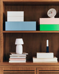 HAY Table Clock, White, white table clock, on a wood bookcase shelf with blue, pink and green storage boxes and a white lamp