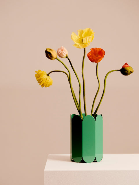 HAY Arcs Vase, Small, Green, green metal flower vase with scalloped sides, holding yellow and orange poppies on a plinth against a pink backdrop