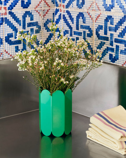 HAY Arcs Vase, Small, Green, green metal flower vase with scalloped sides, with white blossom on a dark counter below blue patterned tiles