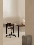 Audo Copenhagen Co Task Chair, Non-Upholstered, dark oak Co Task Chair at a Co Table with a Torso Table Lamp. A gray Volume Side Table is nearby in the minimalist office