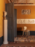 Audo Copenhagen Co Dining Chair, Outdoor, stacked ivory Co Dining Chairs, Outdoor in a mustard room with bas-reliefs, a bust on a pedestal, gray doors and tile floor